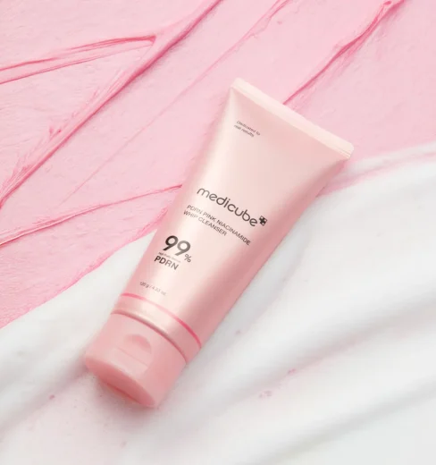 medicube – PDRN Pink Niacinamide Whip Cleanser 120g Medicube PDRN Pink Niacinamide Whip Cleanser 120g tube set against pink and white whipped foam swatches.